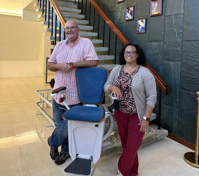 Richard Thompson of Hive Solutions Ltd and deputy chief officer Melissa Ebanks pose with the new powered chair lift (Photo: Cayman Islands Government)